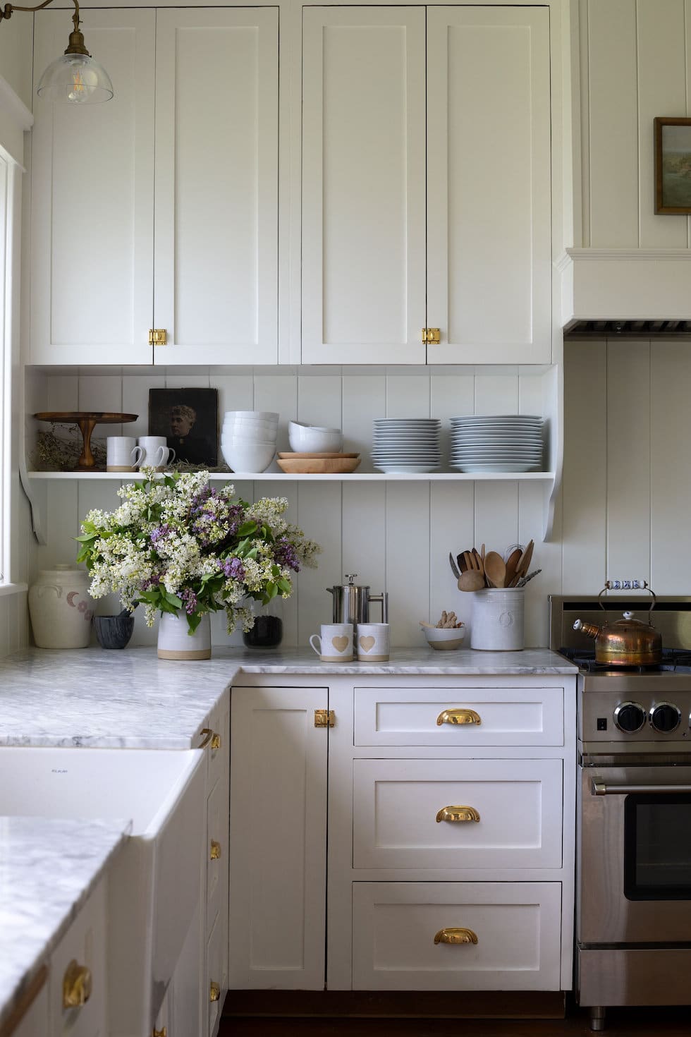 https://theinspiredroom.net/wp-content/uploads/2022/01/white-kitchen-paneled-backsplash-brass-latch-hardware-open-shelves-glass-shade-sconces.jpeg