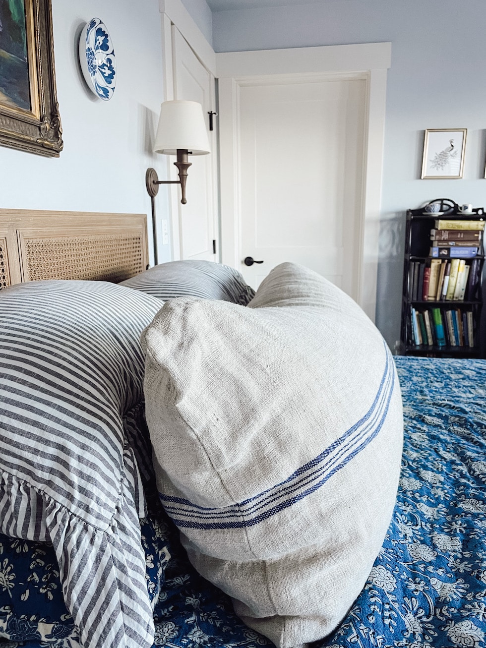 Warm and cozy bedroom interior with big bed, brown bedding, pillows, livid  blue wall, wooden night stand, tray, mug, jug, plaid, vase with dried  flowers and personal accessories. Home decor. Template. Stock