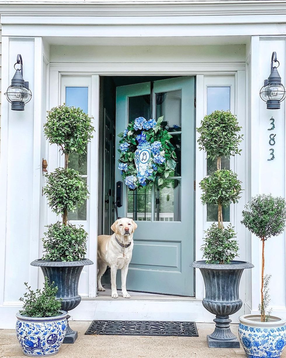 https://theinspiredroom.net/wp-content/uploads/2023/04/blue-white-front-door-porch-hydrangeas-topiaries-coastal-black-lanterns.jpg